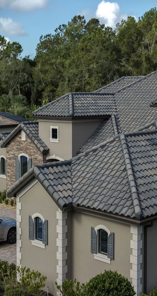 Mediterranean home with grey barrel tile roof, stone veneer, and blue sky